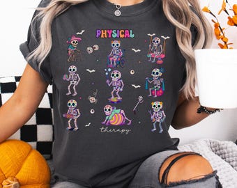 Könnte beinhalten: Dunkelgraues T-Shirt mit farbenfrohen Skelett-Illustrationen, die sich mit Physiotherapie beschäftigen. Das Wort "PHYSICAL" ist in Regenbogenfarben über den Skeletten dargestellt, und "therapy" steht darunter. Das Design hat ein Halloween-Thema.
