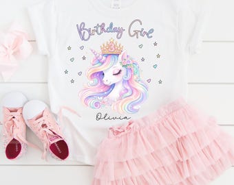 May include: White t-shirt with a colorful unicorn graphic, the text "Birthday Girl", and the name "Olivia". The shirt is paired with a pink tutu skirt and pink sneakers. A perfect outfit for a birthday celebration.