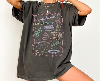 Puede incluir: Una camiseta gris oscuro de gran tamaño con un estampado gráfico de herramientas de terapia ocupacional y el texto "Occupational Therapy".