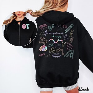 May include: Black zip-up hoodie with a colorful Occupational Therapy design on the back. The design includes various therapy-related illustrations and the words "Occupational Therapy". The front of the hoodie has the letters "OT" in pink and teal.