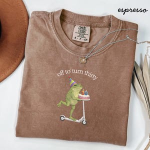 May include: A white ceramic mug with a black handle and the text "But First, Coffee" in a handwritten style. The mug is on a white surface. The mug is approximately 4 inches tall.