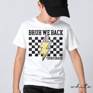 May include: A white t-shirt featuring a black and white checkered pattern background with a yellow pencil shaped like a lightning bolt. The text BRUH WE BACK is printed in black above the graphic, and THIRD GRADE is printed in black below.