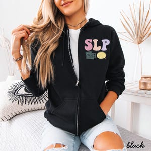 May include: Black zip-up hoodie with the letters "SLP" in pastel colors on the front. The design includes a keyboard and speech bubble graphic. The word "black" is printed in white on the bottom right corner.