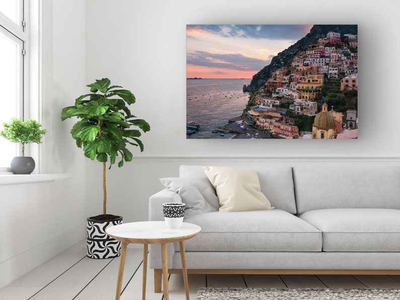 May include: A colorful cityscape built into a cliffside overlooking a body of water. The buildings are a mix of yellow, orange, red, and white, with a large, domed church at the top of the hill. The sky is a soft pink and orange, with clouds in the distance.