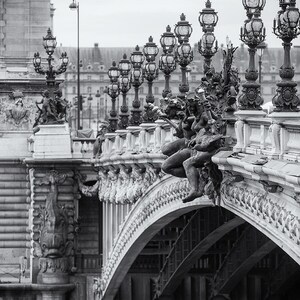 May include: A black and white photo of a bridge with ornate details and lampposts. The bridge is arched and has a stone railing with statues of figures. The bridge is over a body of water.