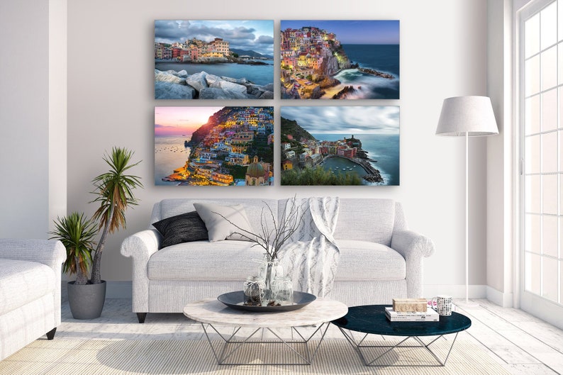 May include: Four framed photographs of a colorful Italian village on a cliff overlooking the ocean. The photos are arranged in a grid pattern on a white wall above a white couch.