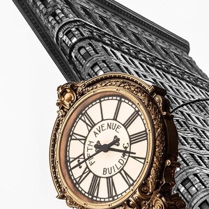 Puede incluir: Una esfera de reloj dorada con números romanos negros y manecillas, sobre un fondo blanco y negro del Flatiron Building en la ciudad de Nueva York. La esfera del reloj dice "Fifth Avenue Building".