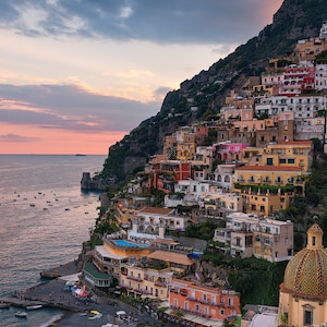 May include: A colorful town built on a steep cliffside overlooking the ocean at sunset. The town is filled with buildings of various sizes and colors, with a large, green-domed church at the bottom of the image.