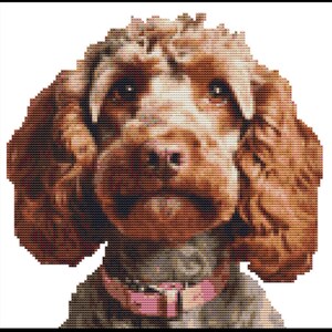 May include: A cross-stitch image of a dog with brown fur and a pink collar. The dog has a fluffy appearance with detailed stitching, showcasing its eyes, nose, and mouth. The background is white, highlighting the dog's features.
