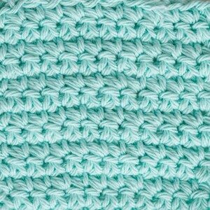 May include: Close-up of a light blue crocheted fabric with a textured pattern.