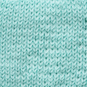 Puede incluir: Primer plano de una tela de punto en color verde azulado claro. La textura muestra un patr&oacute;n claro de puntadas entrelazadas, creando una superficie densa y ligeramente elevada. El hilo parece suave y grueso, lo que sugiere un textil acogedor.