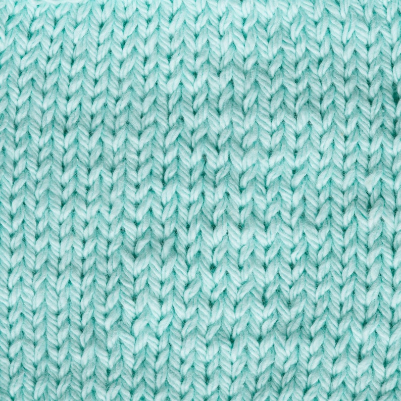 Puede incluir: Primer plano de una tela de punto en color verde azulado claro. La textura muestra un patr&oacute;n claro de puntadas entrelazadas, creando una superficie densa y ligeramente elevada. El hilo parece suave y grueso, lo que sugiere un textil acogedor.