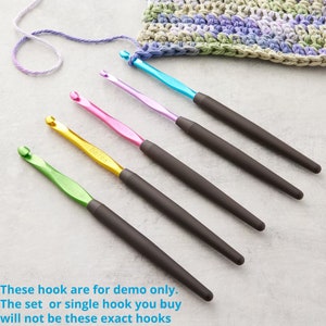 May include: A set of five crochet hooks with colorful metal heads and dark gray ergonomic handles. The hooks are in shades of green, gold, pink, purple, and blue. The text on the hooks reads "Bates". A crocheted swatch and yarn are in the background.