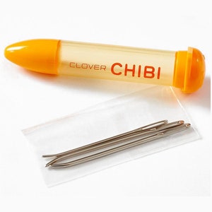 May include: A yellow plastic needle case with the text "CLOVER CHIBI" on the side. The case contains a pack of four silver needles.