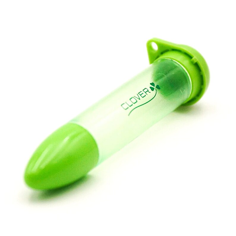 May include: A green and clear Clover needle case. The case is cylindrical with a rounded green tip and a green cap with a small hole. The Clover logo and a shamrock are printed on the clear tube.
