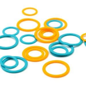 May include: An assortment of colorful rubber O-rings in shades of orange and teal blue. The O-rings vary in size and are scattered against a white background. These are likely used for sealing or as components in various mechanical applications.