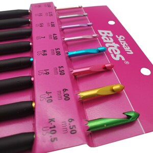 May include: A set of Susan Bates crochet hooks in a pink package. The hooks have black handles and metallic colored heads, with sizes ranging from 2.00 mm to 6.50 mm. The package is labeled with the Susan Bates brand.