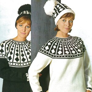 May include: Two women wearing white and black knit sweaters with geometric patterns. Both women are wearing white knit hats with pom-poms.