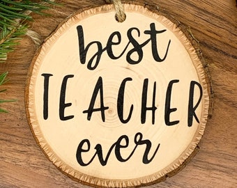 May include: A round wooden ornament with the text "best teacher ever" written in black cursive font.