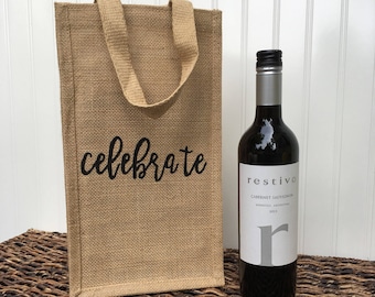 Może przedstawiać: Brązowa torba na wino z juty z czarnym uchwytem i nadrukiem słowa "celebrate" z przodu. Obok torby stoi butelka czerwonego wina.