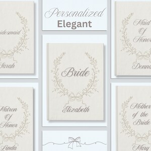 May include: A selection of personalised wedding stationery with elegant designs. Each card displays a name and title such as "Bridesmaid" or "Bride", framed by a floral wreath and bow. The overall theme is classic and sophisticated.