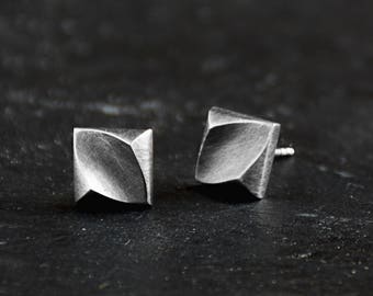 May include: A pair of silver earrings with a geometric, faceted design. The earrings are small and have a textured surface.