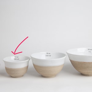 May include: Four white ceramic bowls with a brown rim, lined up from smallest to largest. The bowls are labelled with their capacity in ounces and millilitres. The smallest bowl is 2.5 oz / 100 ml, the next is 10 oz / 300 ml, the next is 18 oz / 550 ml, and the largest is 34 oz / 1 L.