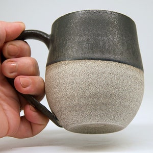 May include: A black and white ceramic mug with a speckled glaze. The mug has a rounded shape and a handle.