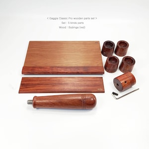 Könnte beinhalten: Ein Gaggia Classic Pro Holzteile-Set aus rotem Bubinga-Holz, bestehend aus fünf verschiedenen Komponenten: einer großen rechteckigen Basis, einem kleineren rechteckigen Streifen, vier zylindrischen Füßen, einem Griff und einem kleinen L-förmigen Werkzeug.
