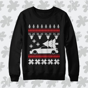 Könnte beinhalten: Schwarzer Weihnachtspullover mit einer weißen Silhouette eines Autos mit einem Weihnachtsbaum darauf. Der Pullover hat ein rotes und weißes Schneeflockenmuster.