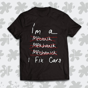 Könnte beinhalten: Schwarzes T-Shirt mit weißem Text, der "Ich bin ein... Mechaniker, Mechaniker, Mechaniker Ich repariere Autos" lautet, wobei die ersten drei Wörter rot durchgestrichen sind.