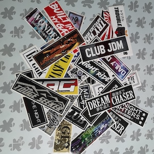May include: A collection of black and white stickers with Japanese text and images of cars, including "CLUB JDM", "NIGHT RIDE", "DREAM CHASER", and "TOUGE SEEKER".