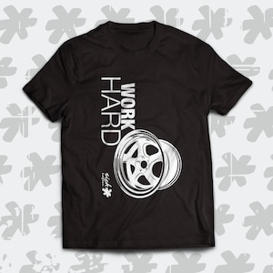 Op de afbeelding: Zwart T-shirt met een witte afbeelding van een autowiel en de tekst "WORK HARD" in een gestileerd lettertype.