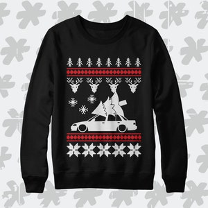 Può includere: Maglione di Natale nero con un'auto bianca che trasporta un albero di Natale in cima. Il maglione ha un motivo rosso e bianco con renne e fiocchi di neve.