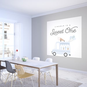May include: A white wall with a blue and white ice cream truck graphic and the text "Lincoln is a Sweet One". There are three balloons in the image. The image is in a dining room with a white table and chairs.