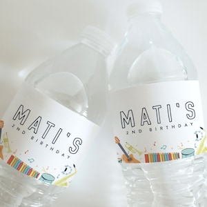 May include: Two clear plastic water bottles with white labels. The labels have a musical theme with a guitar, trumpet, drums, and musical notes. The text on the labels reads "Mati's 2nd Birthday".