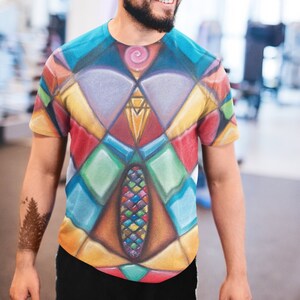 Puede incluir: Un hombre con una camiseta colorida con un patrón geométrico. La camiseta tiene un diseño azul, verde, rojo, amarillo y naranja.