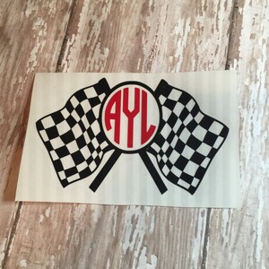 May include: A white sticker with two black and white checkered flags crossed behind a red circle with the letters AYL in white.