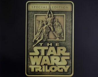 Könnte beinhalten: Ein schwarzes und goldenes Poster, das die Star Wars Trilogie auf RCA Victor Schallplatten bewirbt. Das Poster zeigt eine goldene Plakette mit einem Relief von Luke Skywalker, Prinzessin Leia, Han Solo und R2-D2. Der Text auf dem Poster lautet "Die Star Wars Trilogie" und "Drei Gründe, warum sie Stereos herstellen."