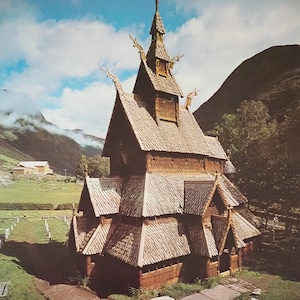 Puede incluir: Un póster vintage con la iglesia de madera de Borgund en Noruega. La iglesia tiene un tejado de varios niveles y está rodeada de campos verdes y montañas bajo un cielo azul. La palabra "NORGE" se muestra de forma destacada.
