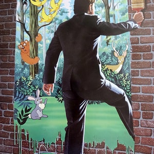 May include: A man in a black suit paints a brick wall with a green paintbrush. The wall is being transformed into a forest scene with a bear, a rabbit, a deer, and birds.
