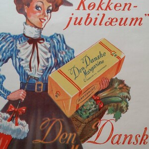 May include: A woman in a blue and white striped dress holds a box of Den Danske Margarine. The box is yellow with red and white stripes. The text on the box reads "Den Danske Margarine" and "Fabrik i Slagelse". The woman is wearing a blue hat with red flowers and a red bow. The text "50 Aars "Kokken-jubil&aelig;um" is printed in red at the top of the image. The text "Den Dansk Margarine" is printed in red at the bottom of the image. The text "Grundlagt 1900 - Stadig Dan" is printed in black at the bottom of the image.