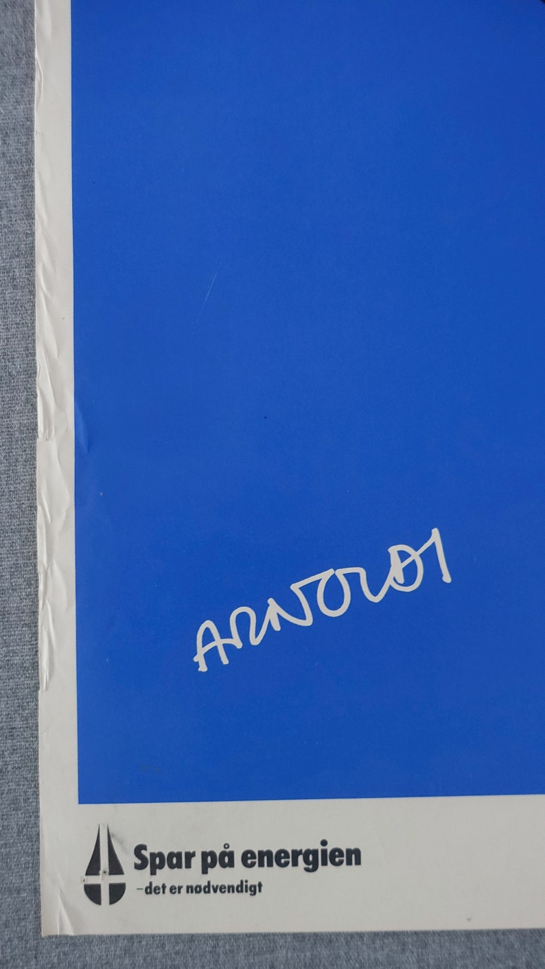 May include: A blue poster with white text that reads "Spar p&aring; energien - det er n&oslash;dvendigt". The poster has a white drop of water with a cross in it. The poster is signed "Anjou" in white.