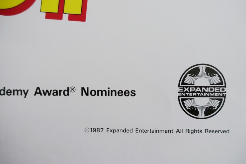 May include: Black and white logo for Expanded Entertainment. The logo features a circle with a stylised design of three hands reaching out. The text "Expanded Entertainment" is printed in white inside the circle.