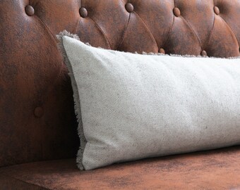 May include: A white throw pillow with a frayed edge sits on a brown leather couch.