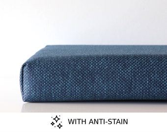 May include: Close-up of a rectangular, upholstered cushion in a deep teal color. The fabric has a woven texture and is labeled "WITH ANTI-STAIN". The cushion is likely for furniture, offering a modern aesthetic.