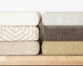 May include: A stack of six rectangular cushions featuring various fabric textures and colors. The left column includes a solid cream textured cushion, a beige patterned cushion, and a solid beige cushion. The right column features a light gray speckled cushion, a dark brown corduroy cushion, and a solid olive green textured cushion.