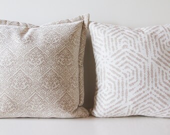 May include: Two decorative throw pillows with a white background and a subtle geometric pattern in a light brown color.