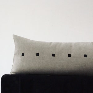 May include: A long, rectangular, light gray linen pillow with a row of black squares down the center.