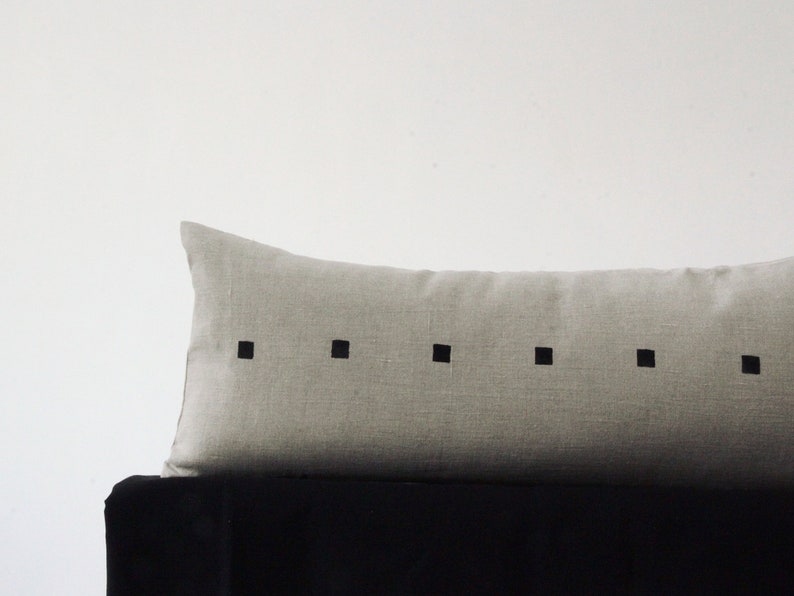 May include: A long, rectangular, light gray linen pillow with a row of black squares down the center.